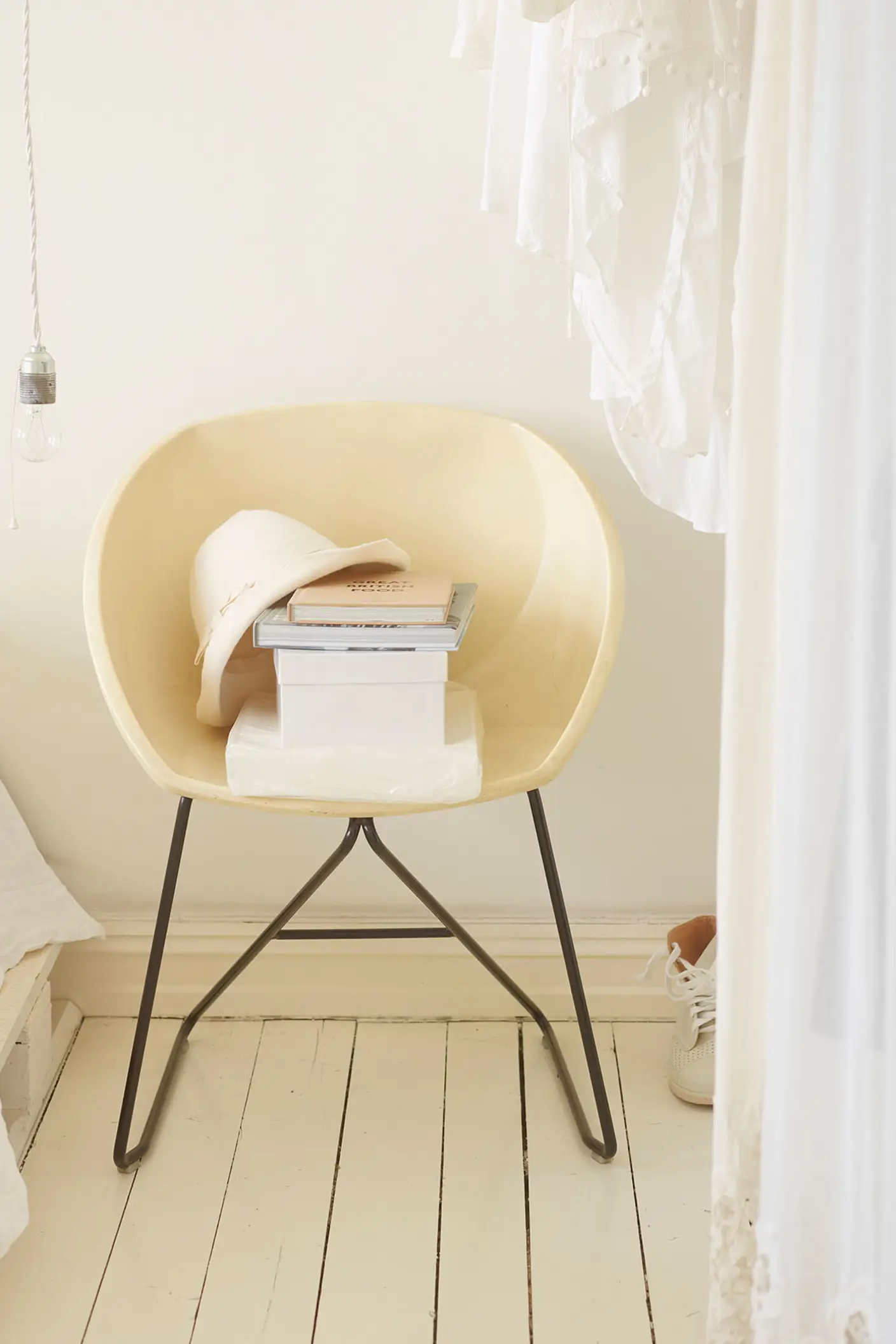 Krämfärgad stol med en hög böcker och en hatt, omgiven av mjuka vita textilier i ett ljust och luftigt rum, målat med Jotun 1624 Lätthet.