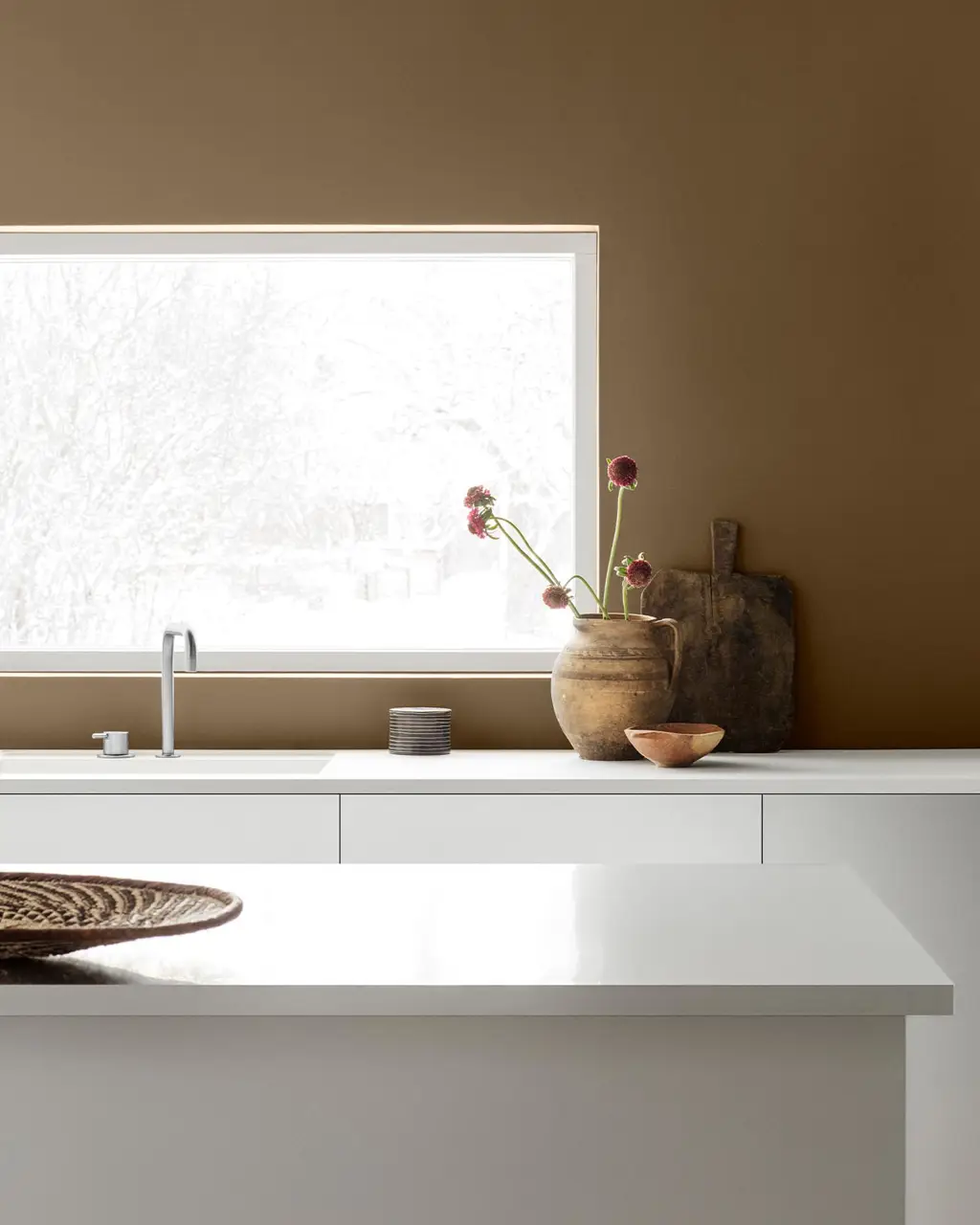 Minimalist kitchen with white cabinets and decor against a golden brown wall painted with the Jotun colour 10963 Golden Bronze.