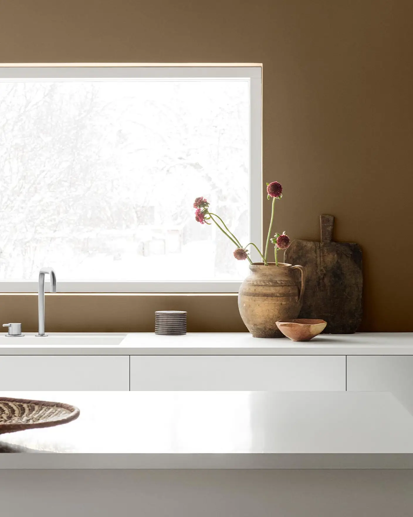 Minimalist kitchen with white cabinets and decor against a golden brown wall painted with the Jotun colour 10963 Golden Bronze.