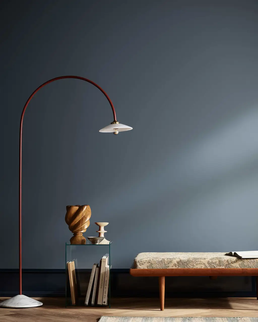 En stue med blå vegger i Jotun 4638 Byge med en høy gulvlist malt mørkere blå i Jotun 4403 Midnight Blue, med en buelampe, et sidebord og en benk