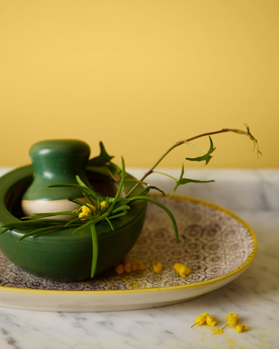 A green ceramic mortar with fresh greenery sitting on a patterned plate against a wall painted in Jotun 8054 Sunny Spot