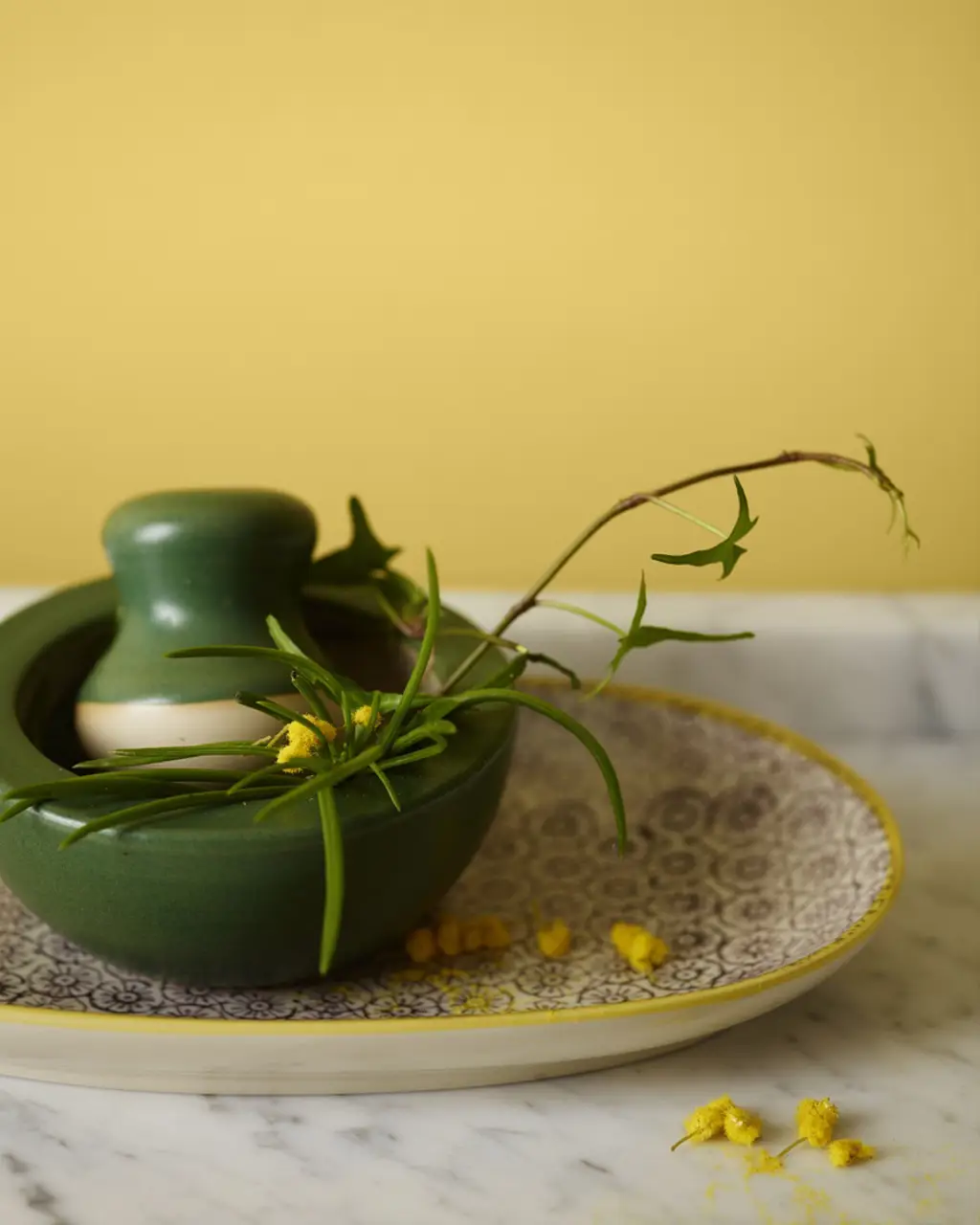 A green ceramic mortar with fresh greenery sitting on a patterned plate against a wall painted in Jotun 8054 Sunny Spot