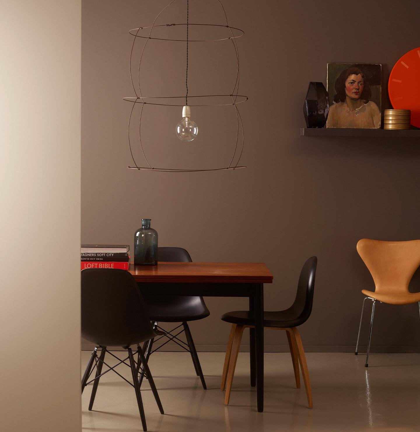 En stemningsfull spisestue med en dempet, brun vegg malt med Jotun 10249 Sober, med mykt lys og utvalgte kunstverk og gjenstander. Aksentveggen foran er malt med Jotun 0553 Chino.