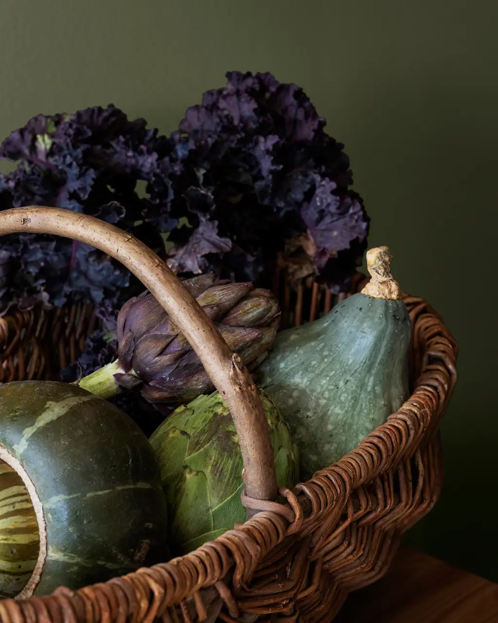 A basket filled with fresh vegetables like artichokes and kale, placed against a rich, yellowish green wall painted with Jotun 8575 Natural Green.