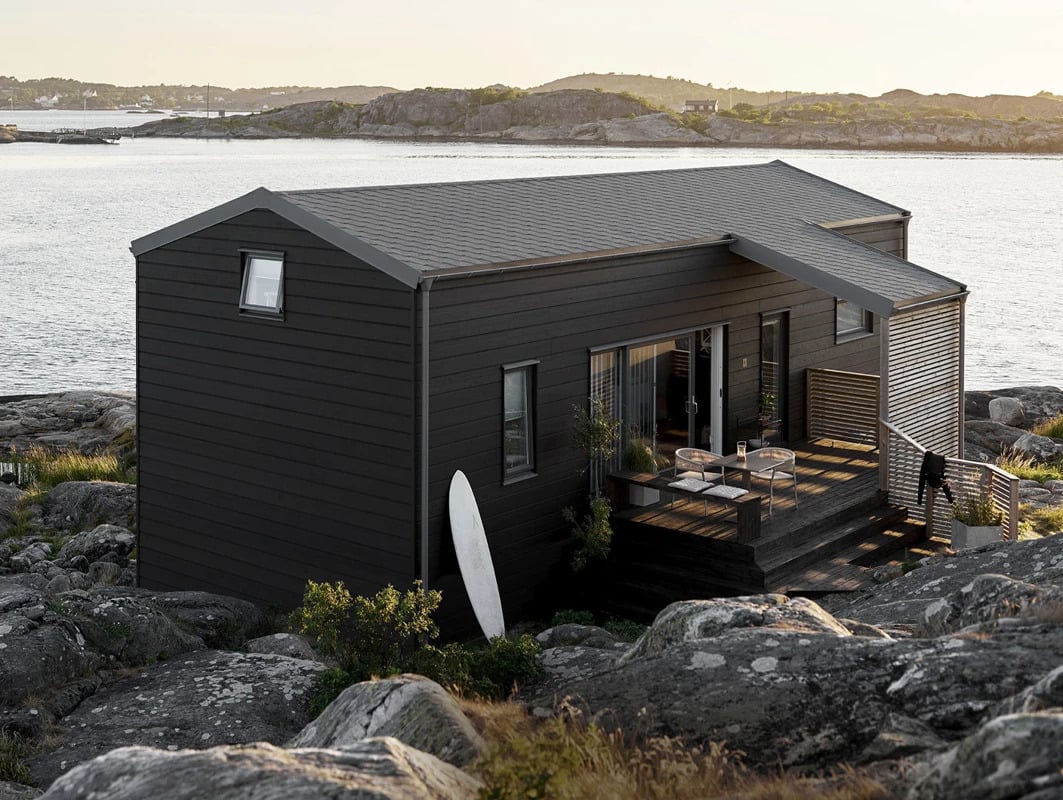 Brunsort hytte i havgapet med surfebrett stående ved veggen