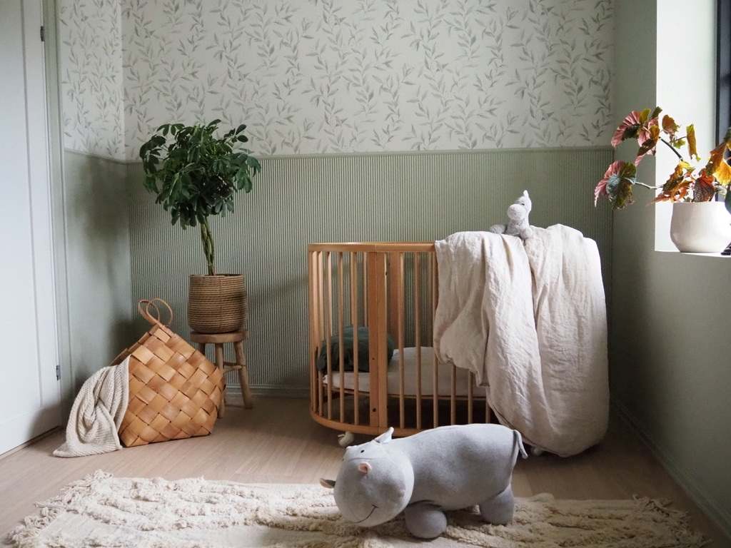 Lysegrønt babyrom i Jotun Pale Linden, flodhest-bamse i front og brun seng fra Stokke helt innerst