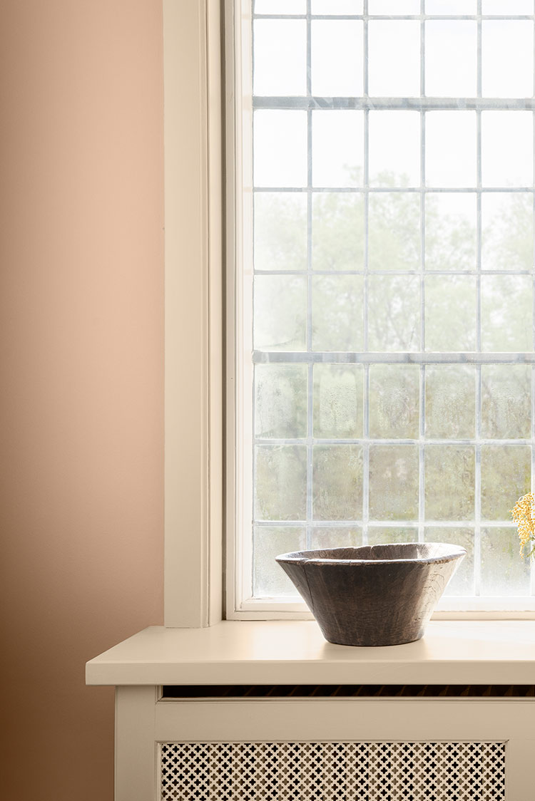 Keramikkskåler og en vase med blomster på en vinduskarm med rutet vindu i bakgrunnen og pudderrosa vegg malt i Jotun 12179 Embrace