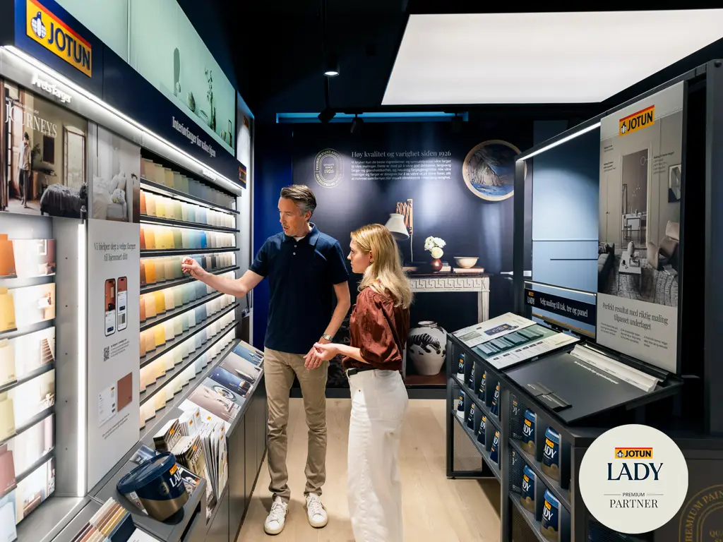 Butikkselger og kunde foran Jotun fargesenter i LADY Premium Partner butikk med logo nede i høyre hjørne.