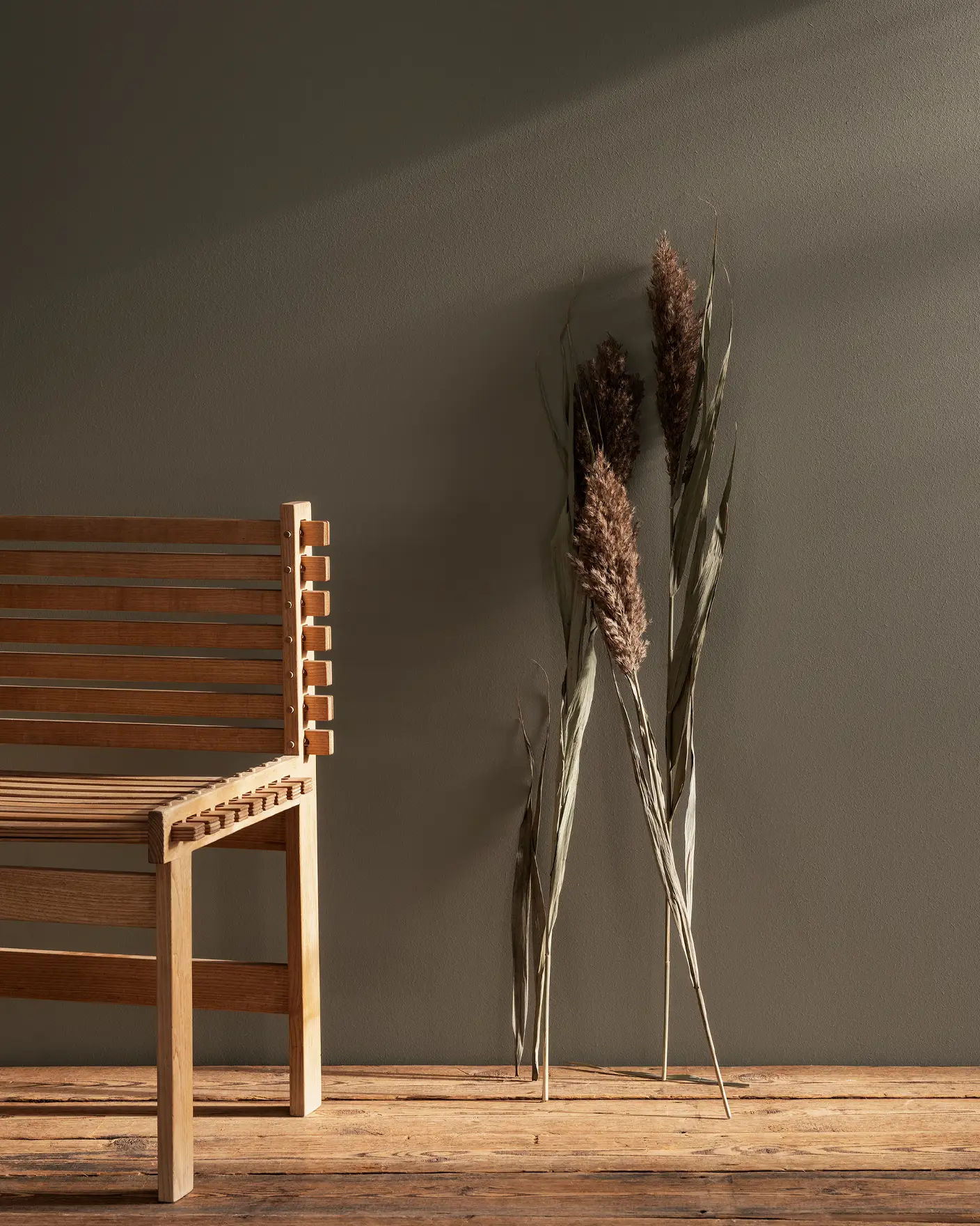 Träbänk i minimalistisk design bredvid torkat gräs mot en neutral vägg målad Jotun 11012 Rustic Brown.