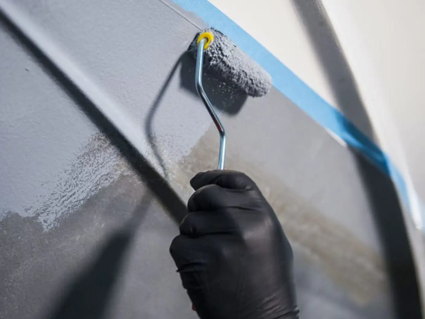 Hånd med sort hanske holder malingsrulle og påfører grunning av båt med produkter fra Jotun