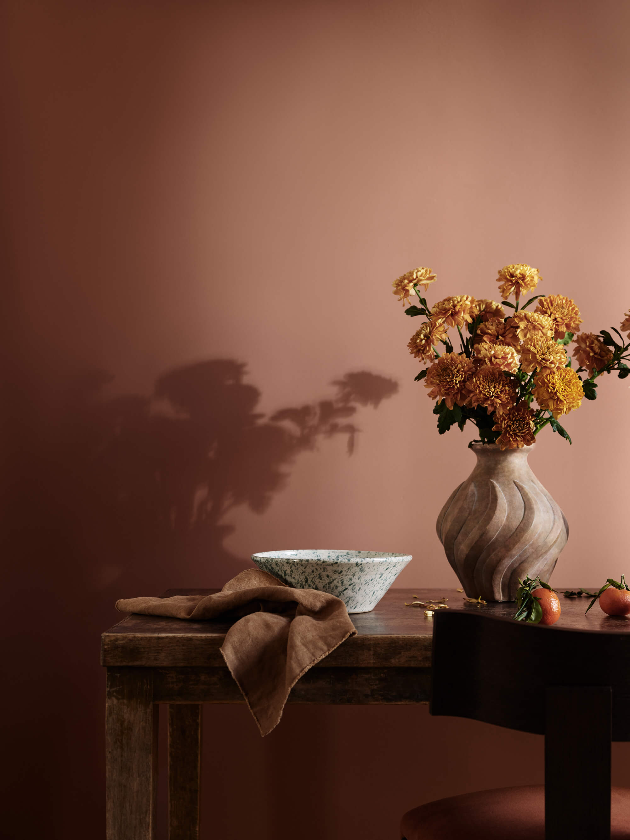 Et rustikt træbord med en skål og blomster i en vase foran en varmt rød væg malet i Jotun 20118 Amber Red.