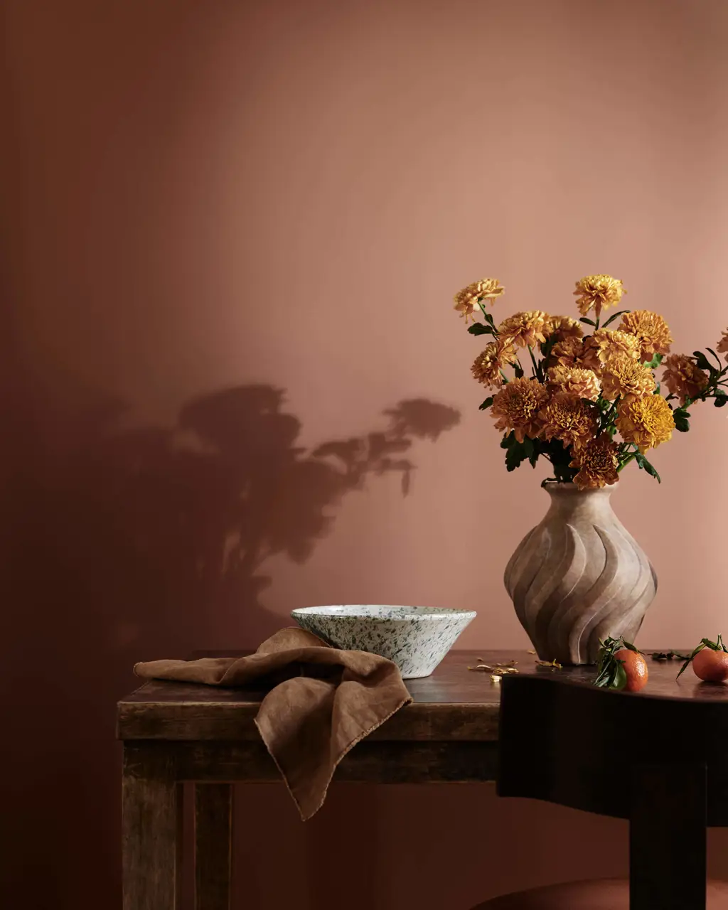 Et rustikt trebord med en skål og blomster i en vase mot en varmt rød vegg malt i Jotun 20118 Amber Red