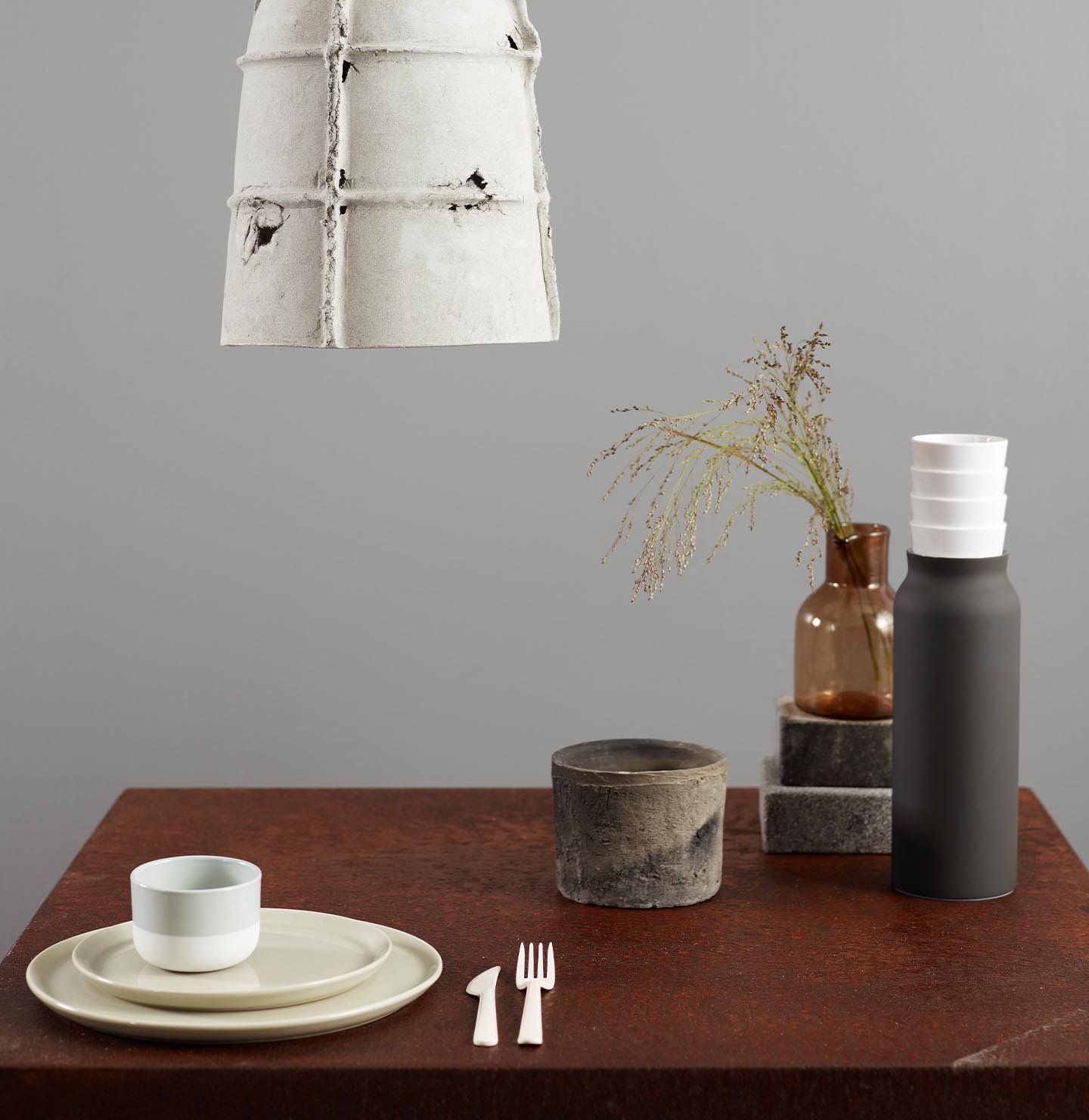 En betonglampa och ett bord dukat med porslin och torkat gräs, mot en mjuk industriell grå vägg målad med Jotun 5343 Industriell Grå.