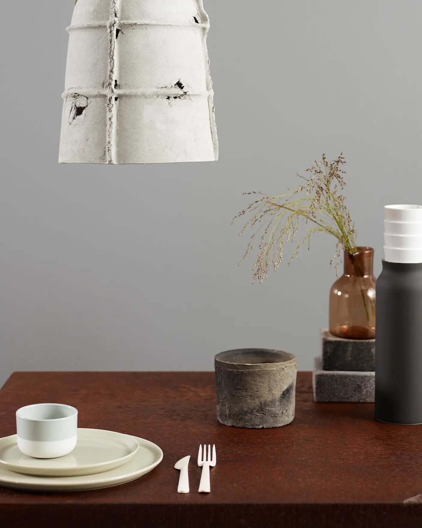 En betonglampa och ett bord dukat med porslin och torkat gräs, mot en mjuk industriell grå vägg målad med Jotun 5343 Industriell Grå.