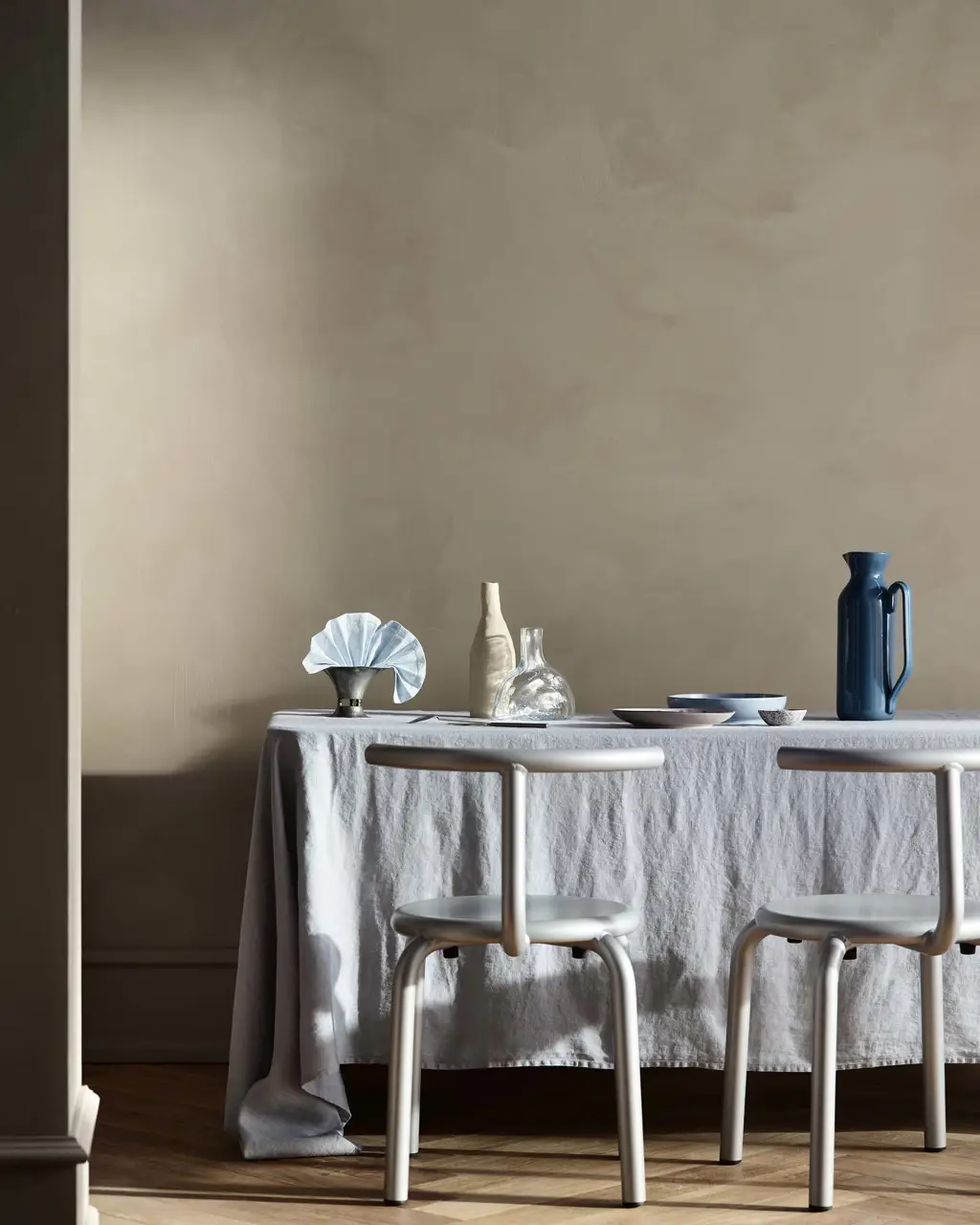 Et spisebord med blå og klare glaskander foran kalkmalede, beige vægge i Jotun 10966 Almond Beige, malet med LADY Minerals.