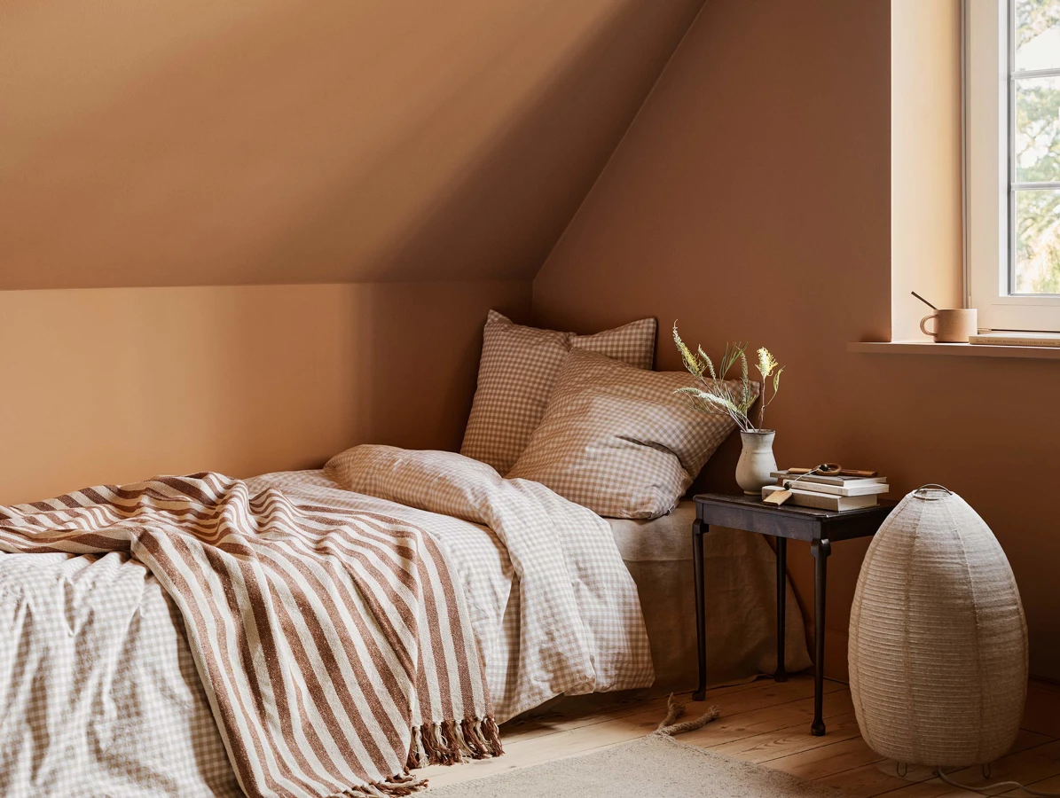 En seng i et soverom malt i okerfargen Ochre Clay fra Jotun