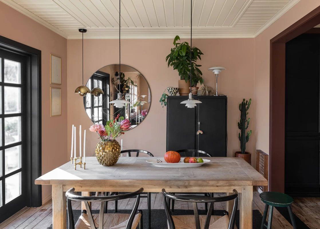 Spisestue med rosa vegger malt i Jotun Pink Ambience, beige tak malt i Jotun Soft Dunes, døråpning til kjøkken malt i rødt Jotun Sophisticated Red og terrassedør malt i Jotun LADY Dempet Sort.