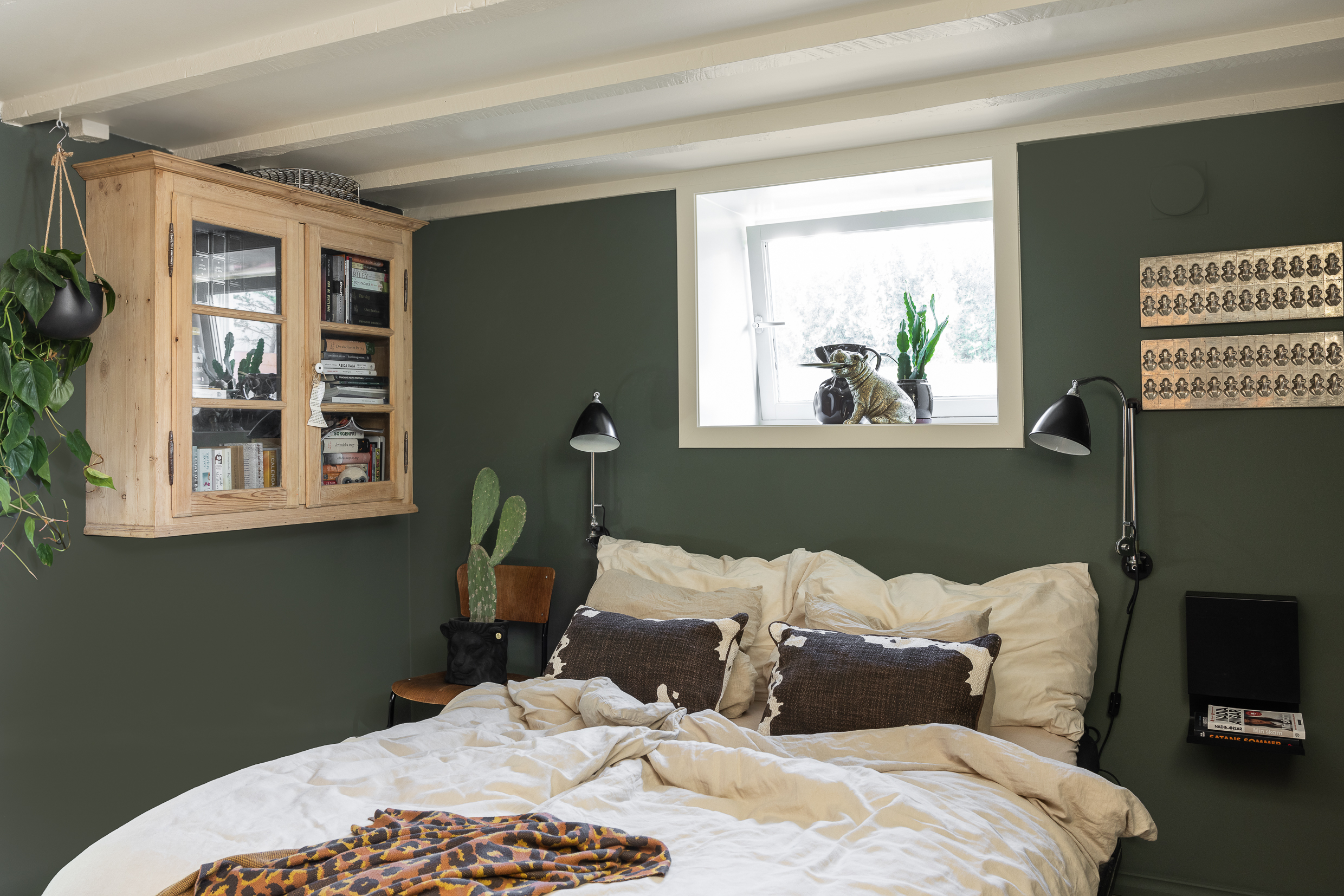 Soverom i underetasje med beige tak i Jotun Soft Dunes og mørke grønne vegger malt i Jotun Northern Mystic, industriell og personlig stil på interiøret og flere grønne planter.