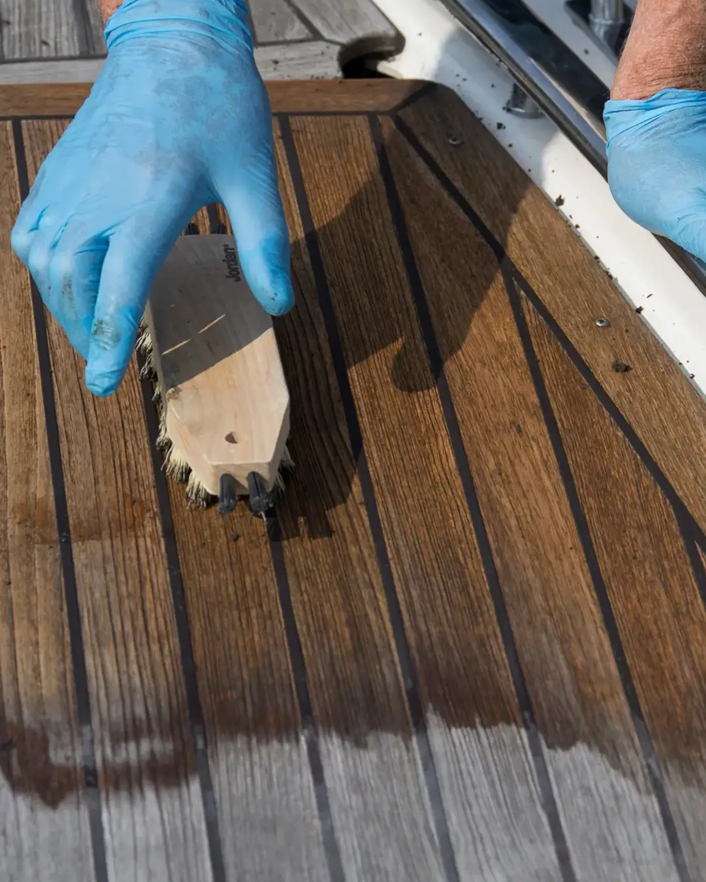 Vasking av teakdekk på båt med skrubb og hansker på