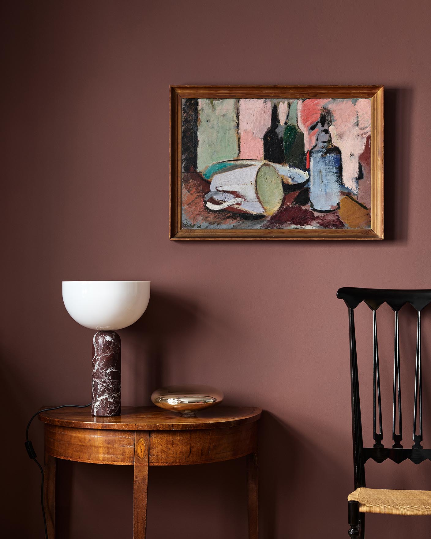 Wooden side table with a lamp beneath an abstract painting hanging on a deep red wall painted with the Jotun colour 2951 Sophisticated Red.