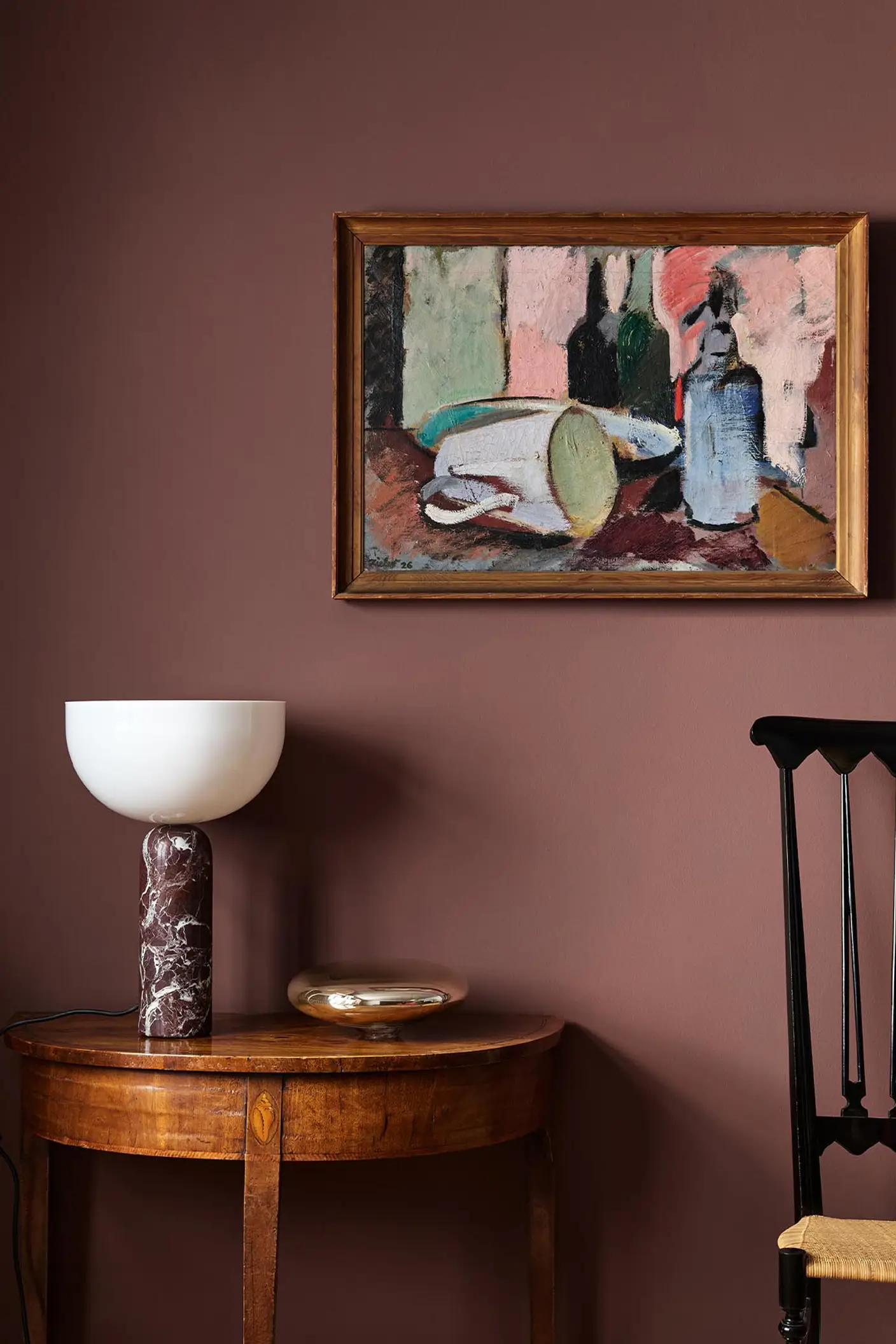 Wooden side table with a lamp beneath an abstract painting hanging on a deep red wall painted with the Jotun colour 2951 Sophisticated Red.