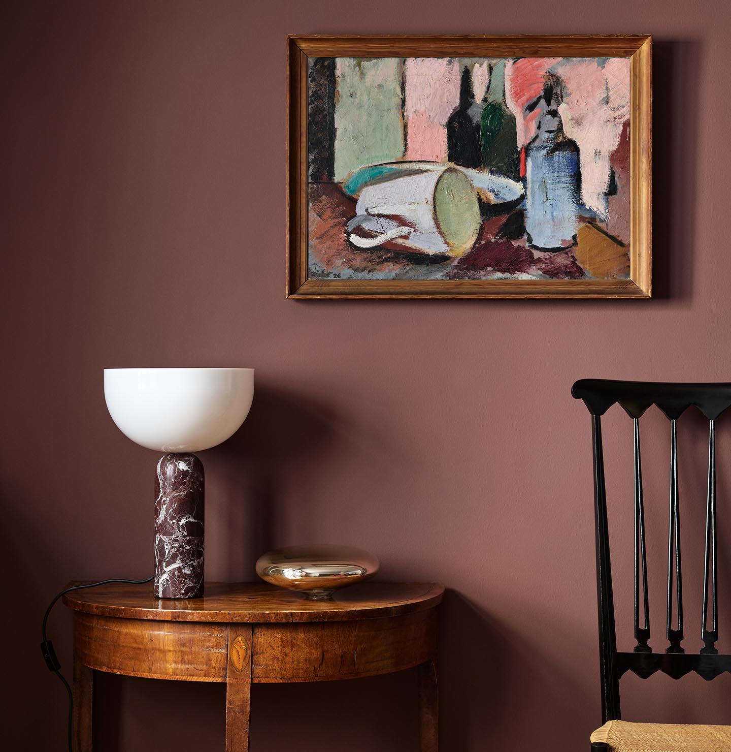 Wooden side table with a lamp beneath an abstract painting hanging on a deep red wall painted with the Jotun colour 2951 Sophisticated Red.