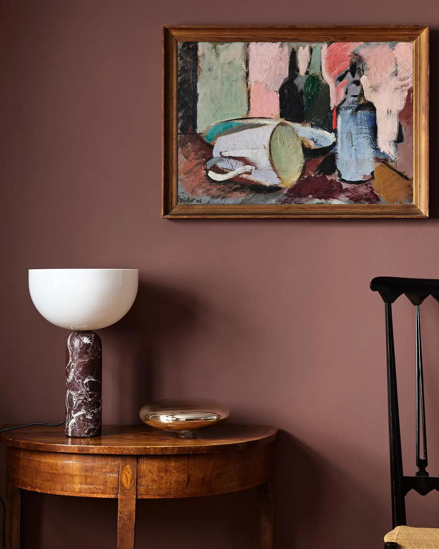 Wooden side table with a lamp beneath an abstract painting hanging on a deep red wall painted with the Jotun colour 2951 Sophisticated Red.