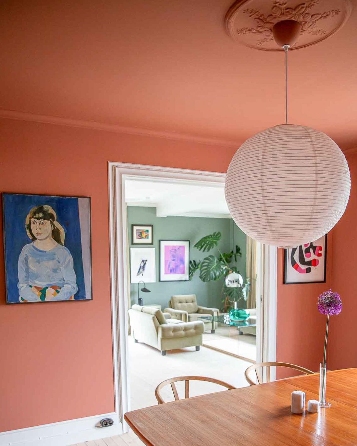 Spisestue med tak og vegger malt i korallrøde Jotun Muted Coral, hvit rislampe i tak over spisebord i teak.