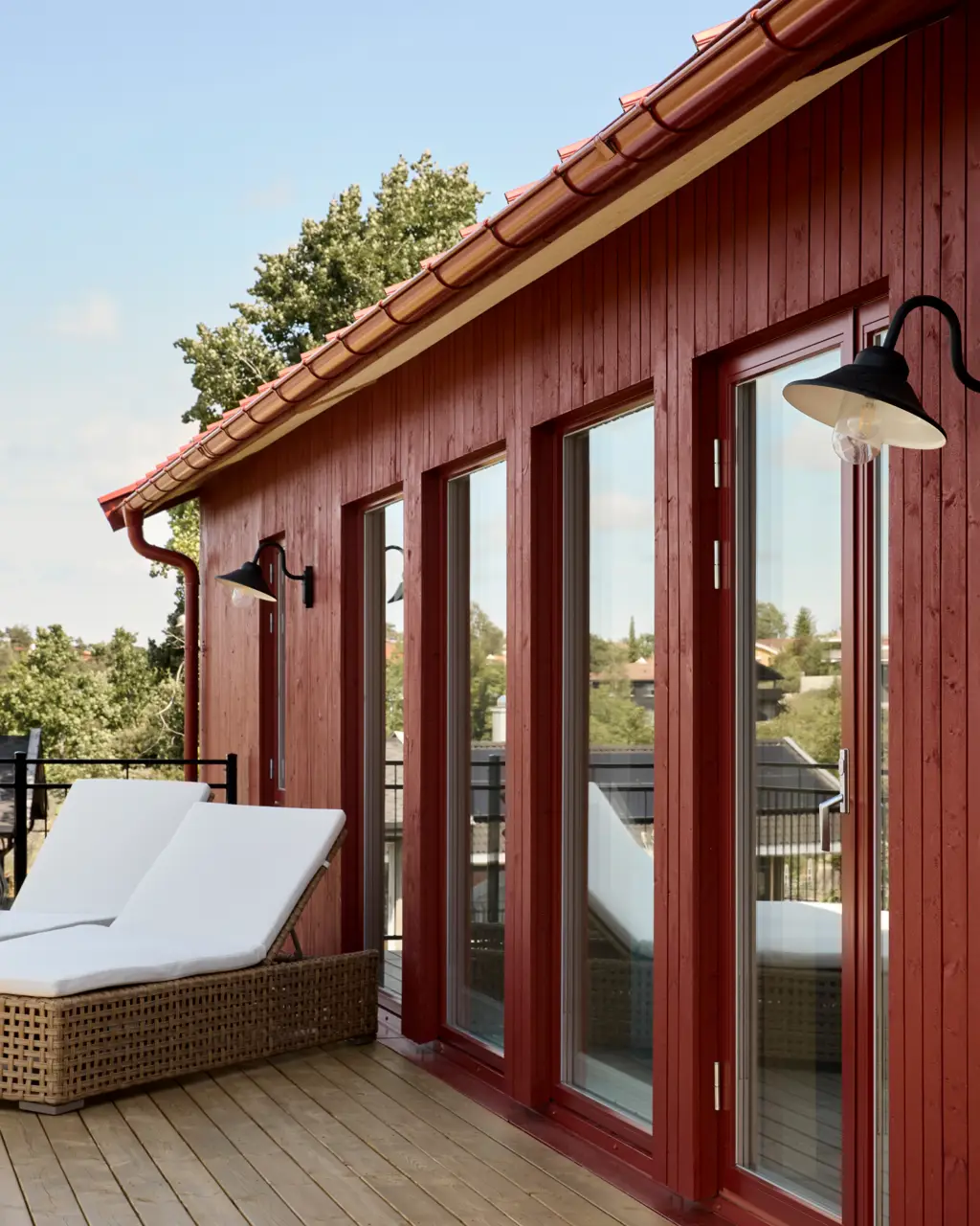 Rødt funkishus malt i Jotun Villvin, solsenger med hvite puter på terrassen foran huset.