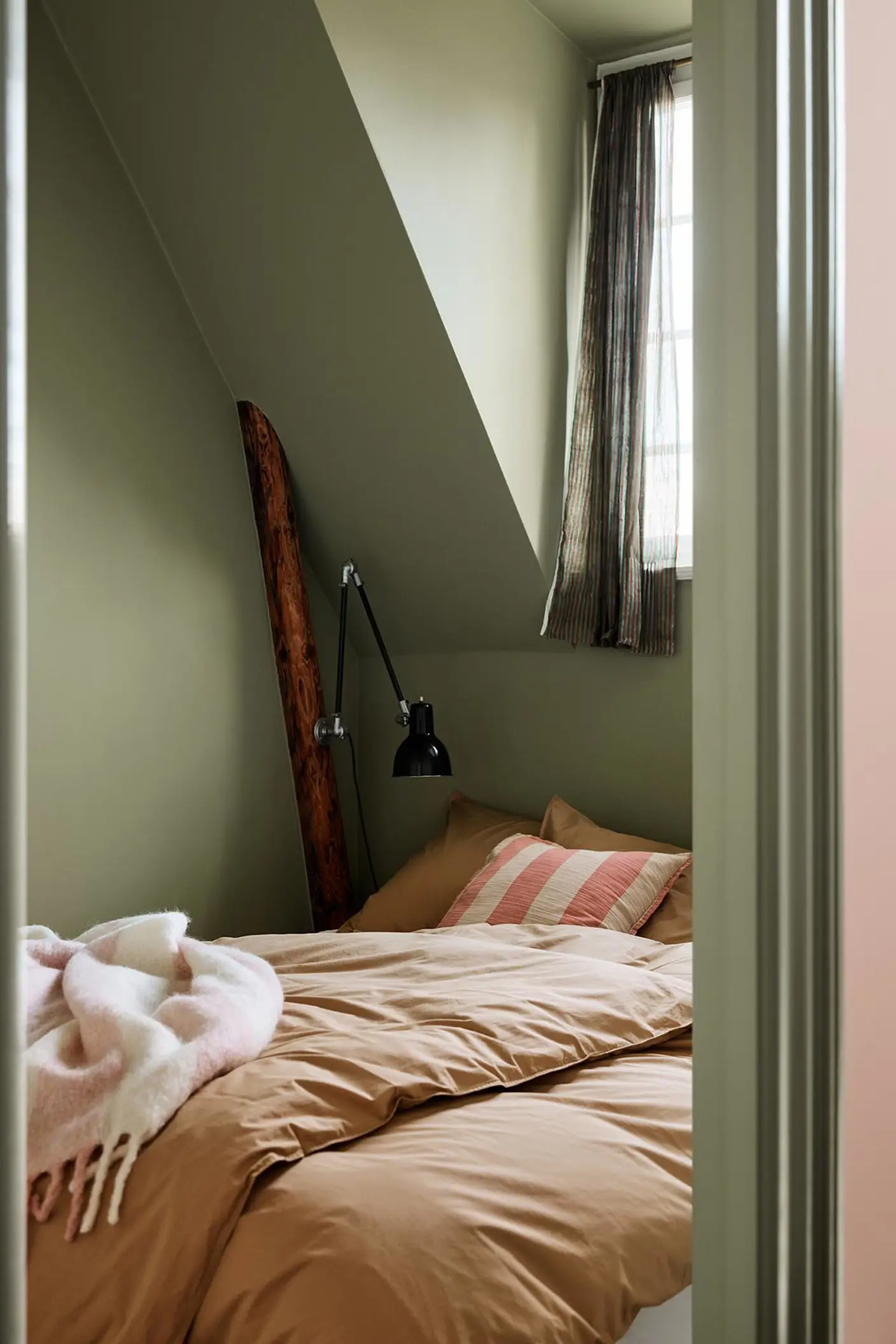 Bedroom with brown bedding and a pink-striped pillow against green painted walls and trims in the Jotun colour 8493 Green Tea.