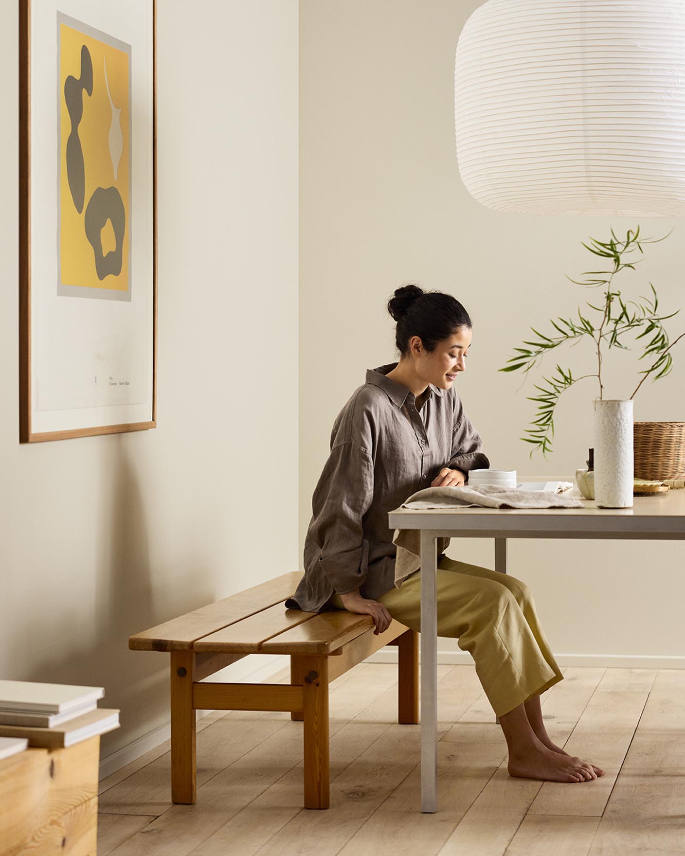 Woman sitting on a wooden bench by a desk with beige walls painted in the colour Jotun 12308 Unbleached.
