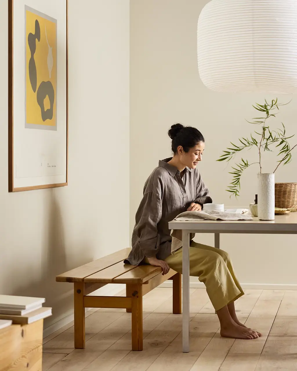 Woman sitting on a wooden bench by a desk with beige walls painted in the colour Jotun 12308 Unbleached.