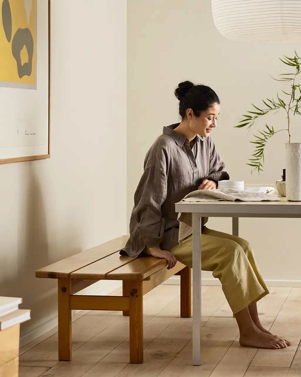 Woman sitting on a wooden bench by a desk with beige walls painted in the colour Jotun 12308 Unbleached.
