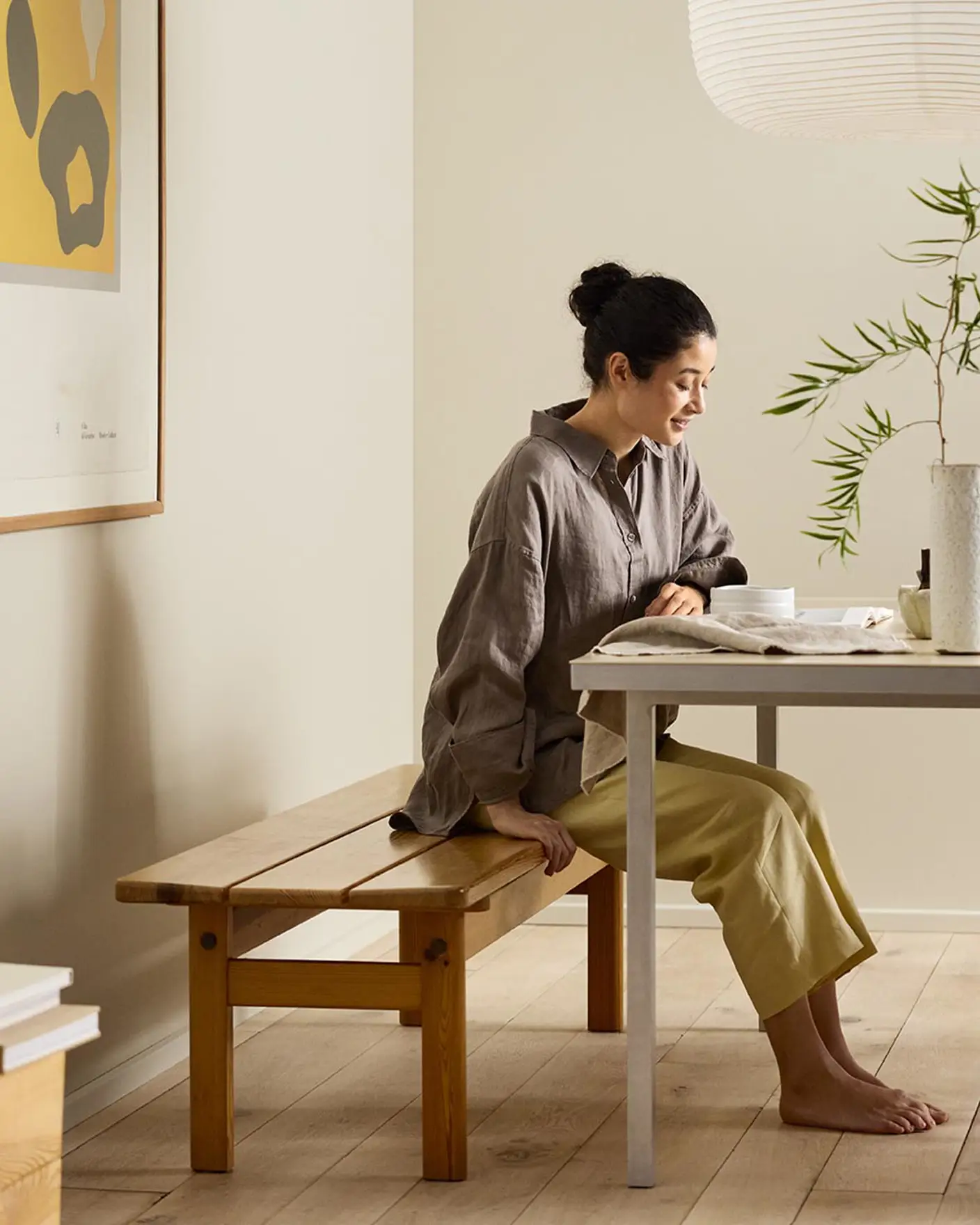 Woman sitting on a wooden bench by a desk with beige walls painted in the colour Jotun 12308 Unbleached.