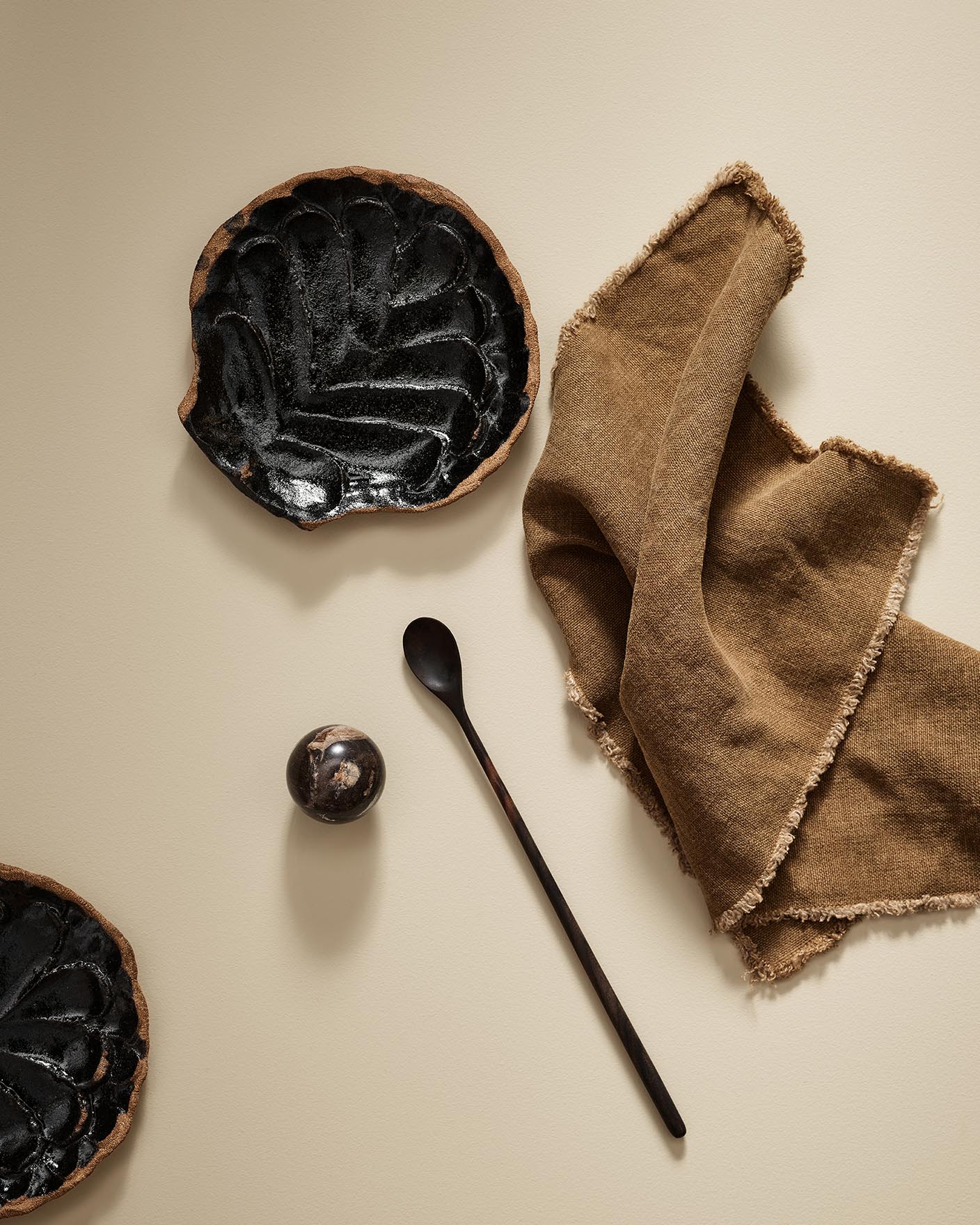 Black ceramic plate with a spoon and brown cloth on a beige surface in the colour 1303 Observe from Jotun.