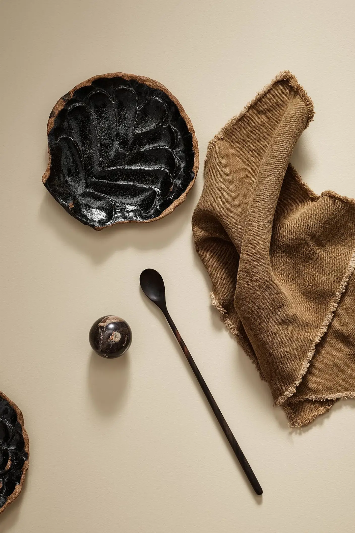 Black ceramic plate with a spoon and brown cloth on a beige surface in the colour 1303 Observe from Jotun.