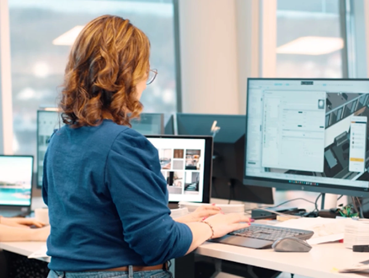 Arkitekt arbeider ved datamaskin på moderne kontor, med designprogram og flere skjermer.