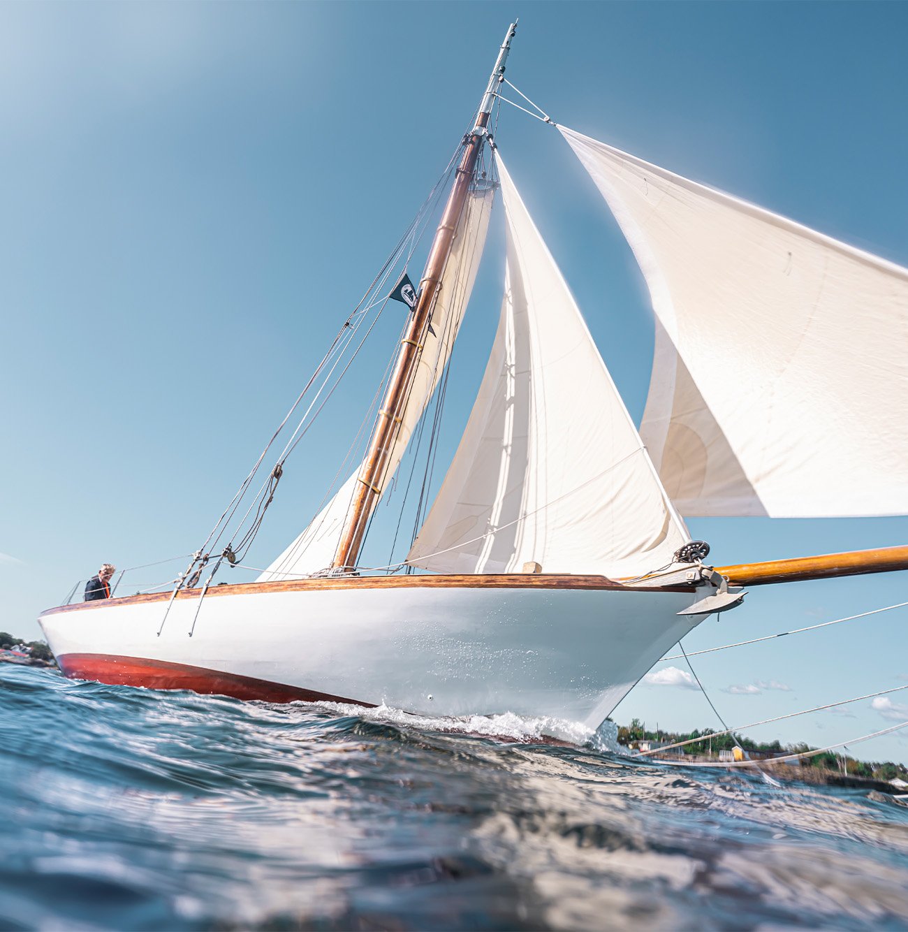 Seilbåt med hvite seil som skjærer gjennom vannet på en klar sommerdag.