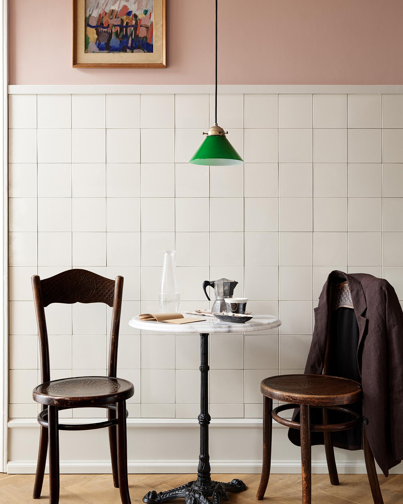 A table and wooden chairs in front of a tiled wall. The upper wall is painted in the soft pink colour Jotun 20362 Pink Ambience. 
