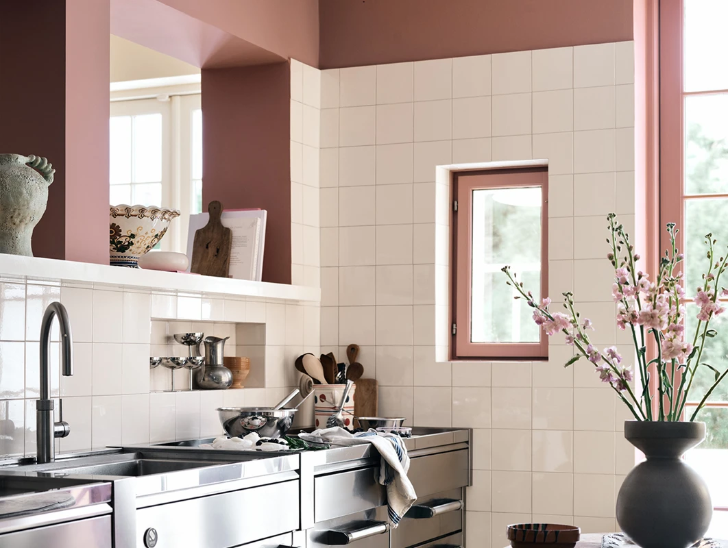 Et kjøkken malt med Jotun 20256 Balmy Pink, Jotun 11365 Morning Glow, og Jotun 11364 Century White med skapdører av stål og hvite fliser på veggene.
