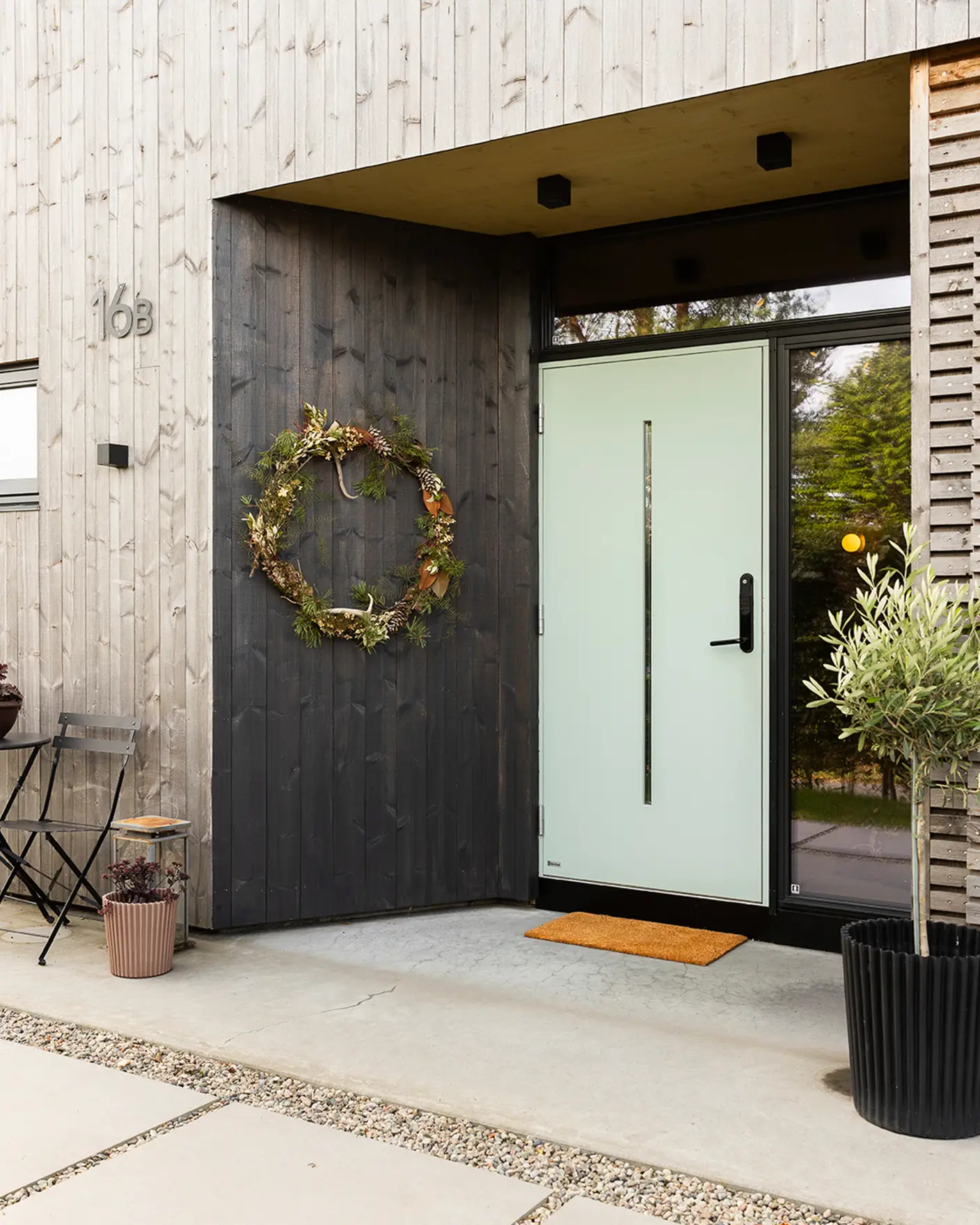 Inngangsparti til moderne funkishus i malmfuru, vegg rundt lysegrønn dør oljet med TREBITT WoodCare i gråsorte Muted Charcoal og tak over dør i gylne Fair Wood.