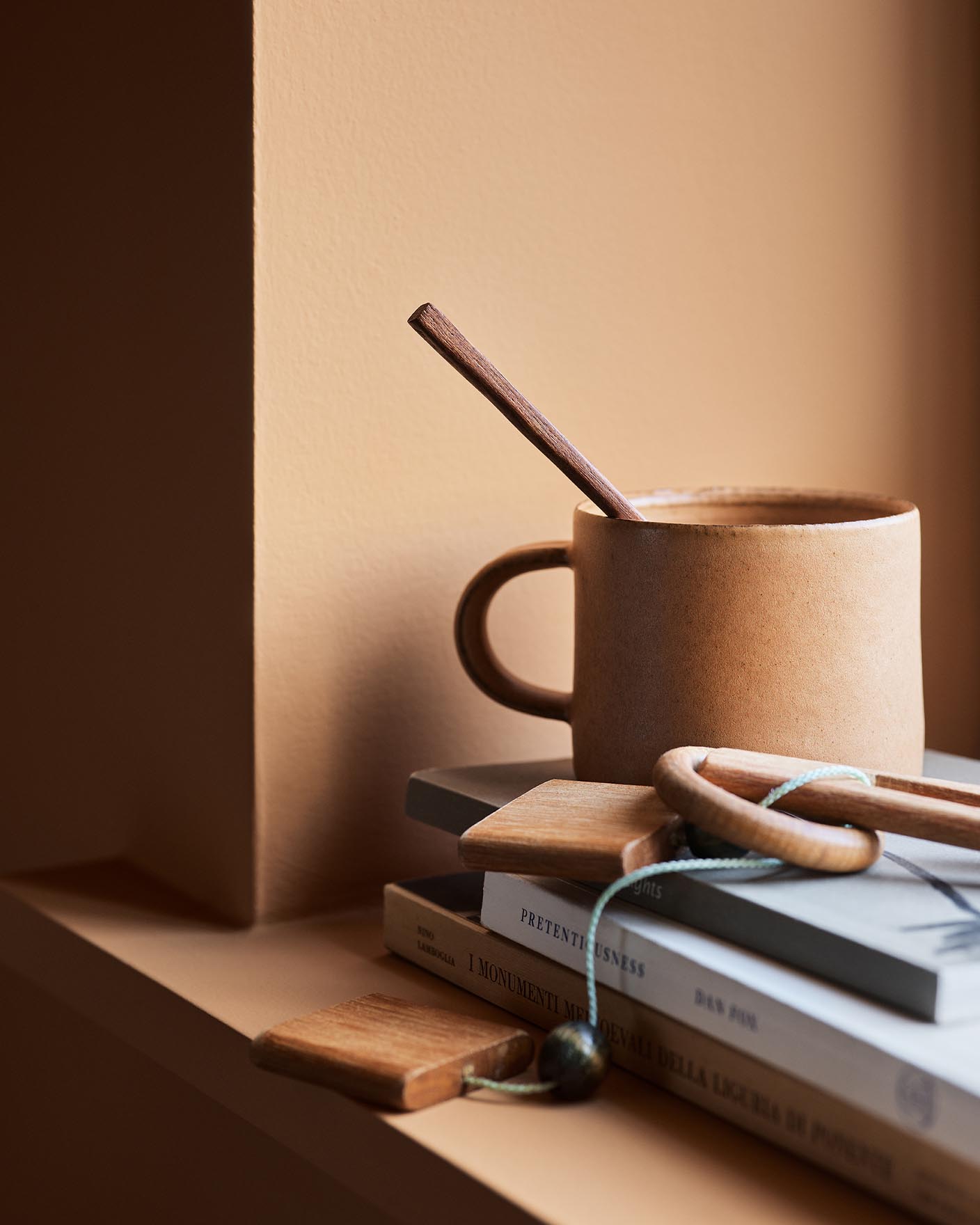 Ceramic mug with a wooden stirrer on stacked books against a ochre wall painted with the Jotun colour 11220 Ochre Clay.