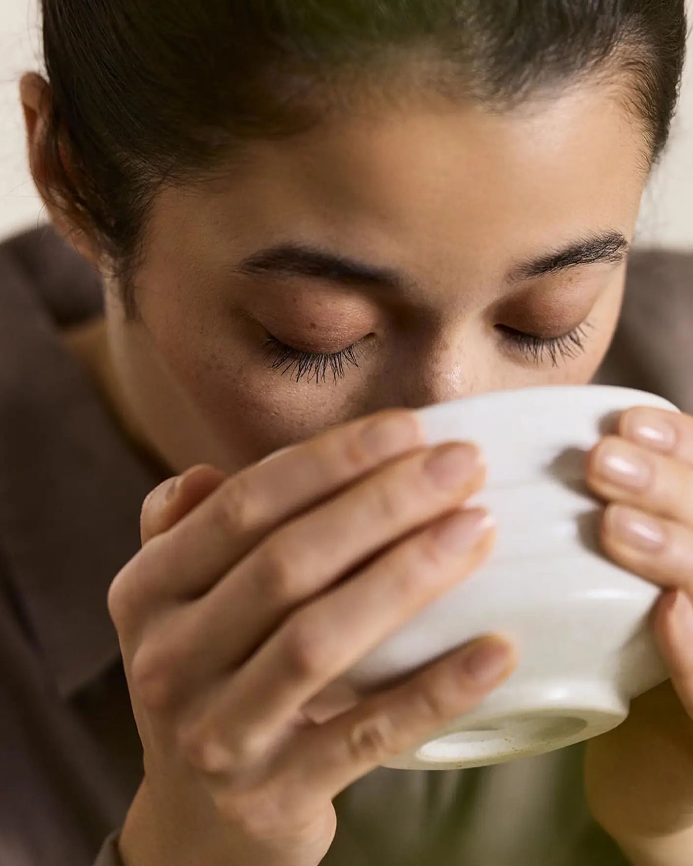 Woman drinking from a cup with a beige background in the colour Jotun 12308 Unbleached.