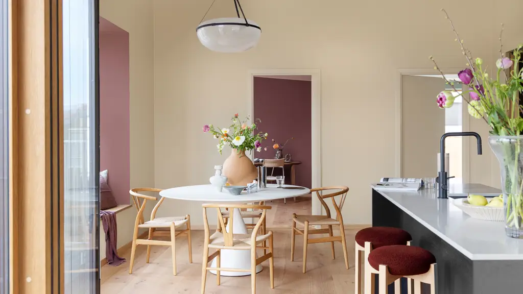 Spisestue med moderne møbler og kjøkkenøy, vegger i myk, gyllen beige malt i JOTUN 1303 Observe, karnapp og rom på innsiden malt i rødt i fargen JOTUN 2951 Sophisticated Red