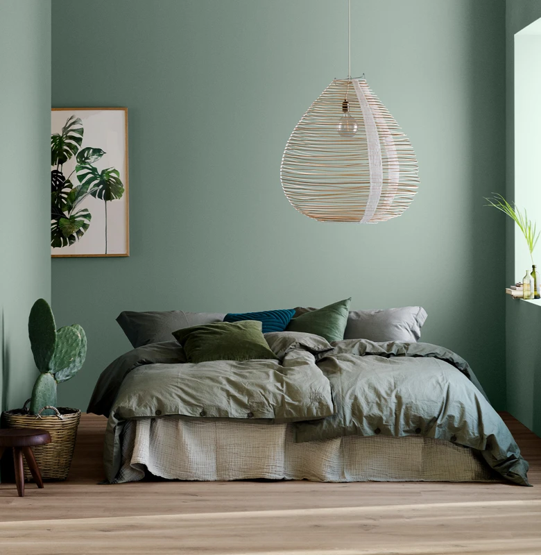 Soverom malt i fargen Soft Teal fra Jotun, oppredd seng, på veggen henger et bilde av en plante og en ved siden av sengen står en kaktus.