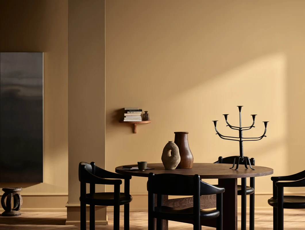 Minimalistisk spiseplass med rundt trebord, svarte stoler, dekorative vaser og lys som faller inn i et stilrent malt i fargen Jotun Kalkoker og Spice Brown