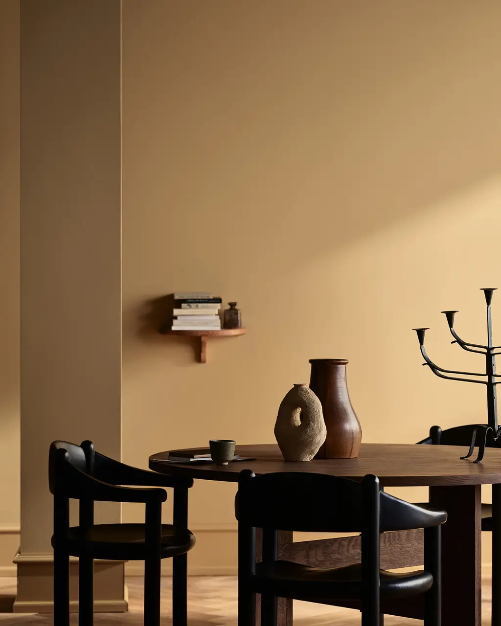 Minimalistisk spiseplass med rundt trebord, svarte stoler, dekorative vaser og lys som faller inn i et stilrent malt i fargen Jotun Kalkoker og Spice Brown