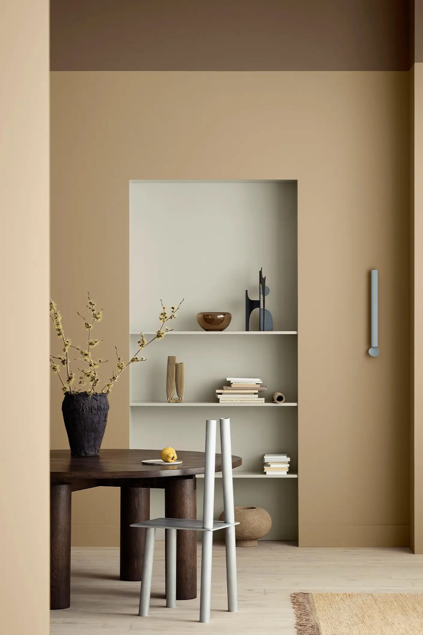 Ett varmt, minimalistiskt matrum med gyllenbruna väggar målade med Jotun 1632 Rock Sugar och inbyggda hyllor målade med Jotun 12075 Soothing Beige, stylade med böcker och keramik.
