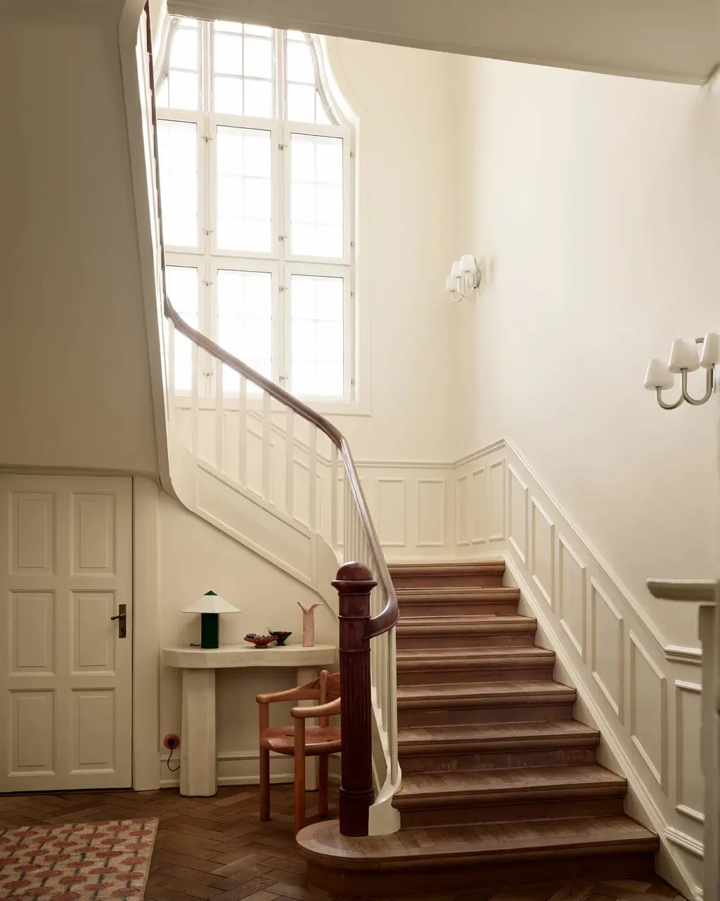 Hallway with Jotun 11365 Morning Glow trim and lower and upper walls. Features a grand wooden staircase leading up