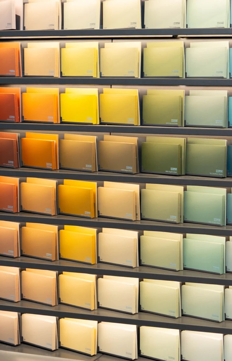 A display of Jotun interior paint color swatches arranged on shelves by shade, ranging from warm oranges and yellows to cool greens